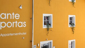Un immeuble jaune avec une enseigne indiquant « ante portas Appartementhotel » et de nombreuses fenêtres ornées de plantes.