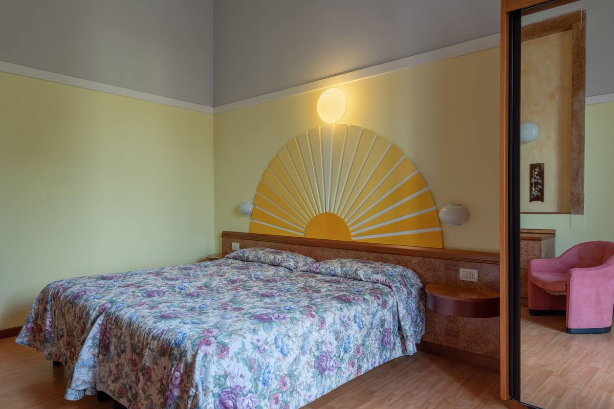 A bedroom with a bed, a nightstand, a mirror, and a chair.