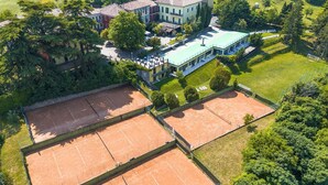 Vista aérea de un complejo de canchas de tenis con edificios cercanos y zonas verdes circundantes.
