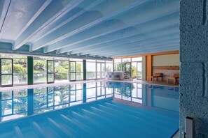 An indoor swimming pool with clear glass walls, a tiled floor, and a seating area with benches. - Park Hotel Jolanda (San Zeno di Montagna)