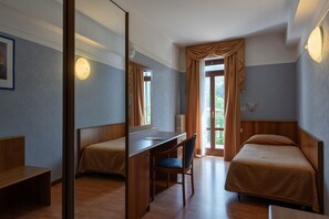 A room with two beds, a desk, and a chair. There is a window with curtains, a radiator, and a wall-mounted light fixture. - Park Hotel Jolanda (San Zeno di Montagna)