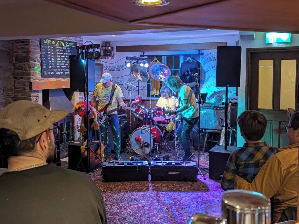 A band performing on a stage with a brick wall backdrop and a menu board to the left.