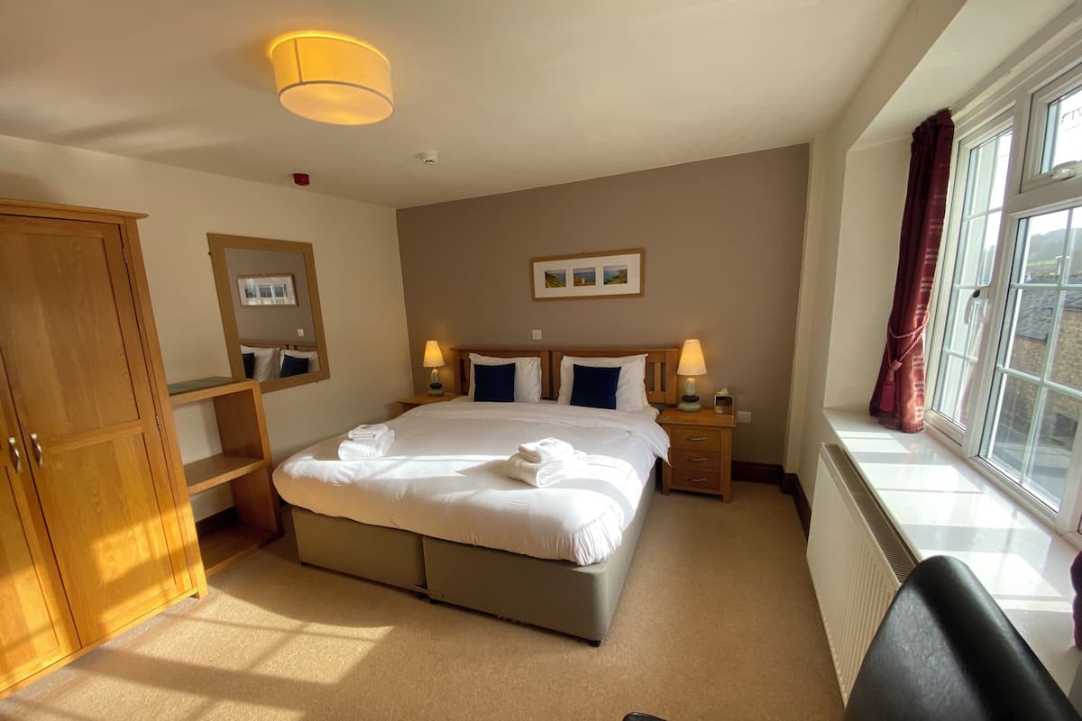 Quarto de hotel bem arrumado com uma cama grande, abajures, guarda-roupa e uma janela com cortinas.