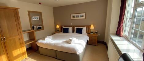 A neatly arranged hotel room with a large bed, bedside lamps, a wardrobe, and a window with curtains.