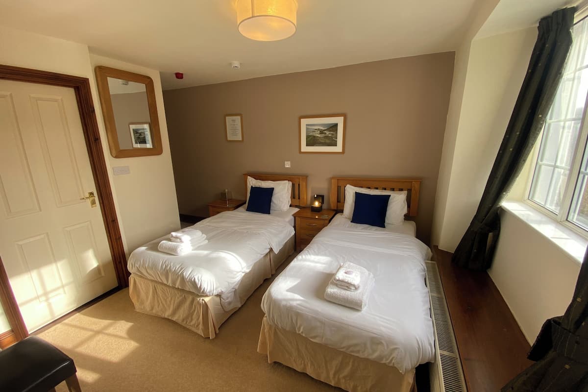 Quarto de hotel com duas camas, um espelho grande, uma janela com cortinas e um radiador.
