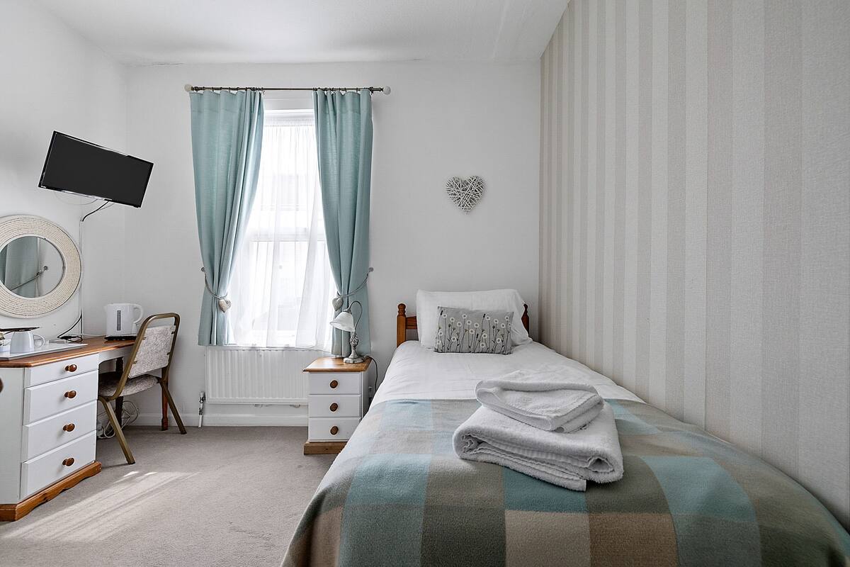 A bedroom with a bed, a desk, a chair, a television, and a window with curtains.