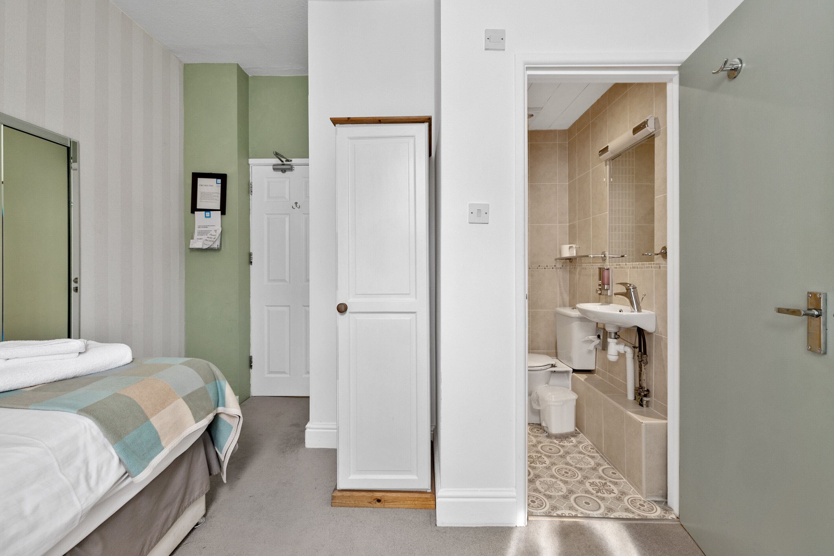 A hotel room with a bed, a bathroom with a sink and toilet, and a door leading to another room.
