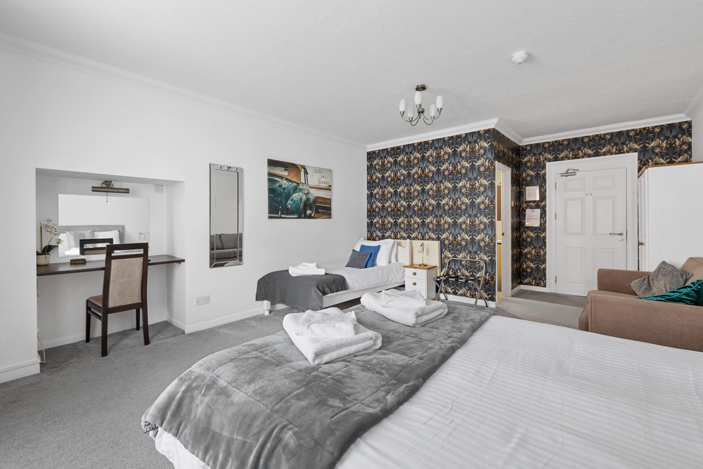 A bedroom with a bed, a desk, a chair, a nightstand, and a door.