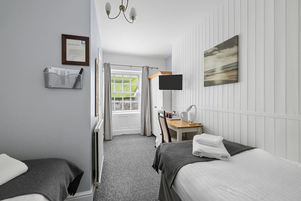 A hotel room with two beds, a desk with a chair, a flat-screen TV, and a window with curtains.