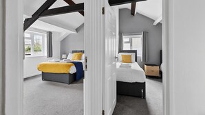 A bedroom with two beds, a window, and a door leading to another room. - Imperial Plymouth (Plymouth)