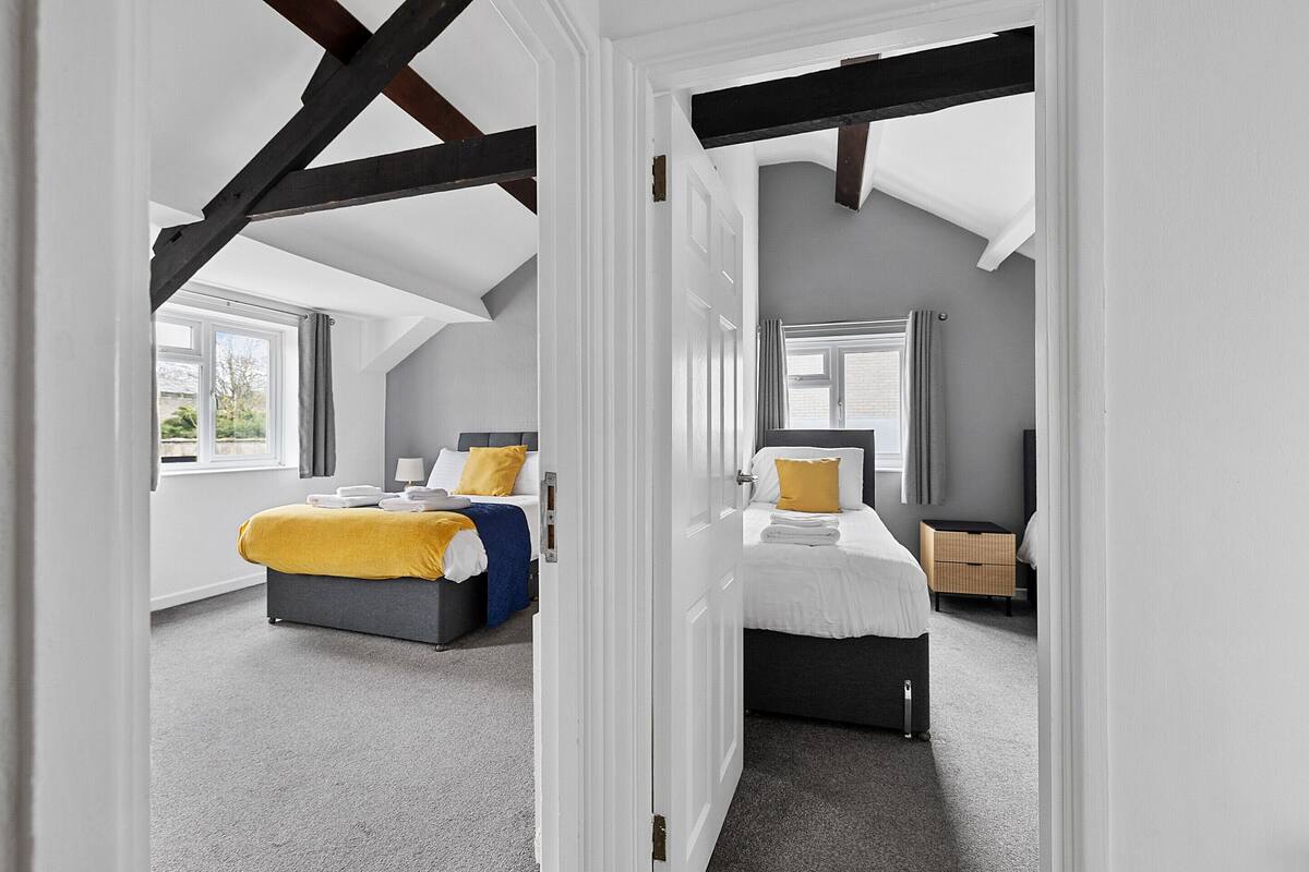 A bedroom with two beds, a window, and a door leading to another room.