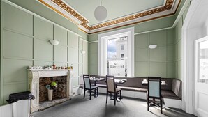 A room with a fireplace, a dining table with chairs, a bench, and a view of the street through a large window. - Imperial Plymouth (Plymouth)