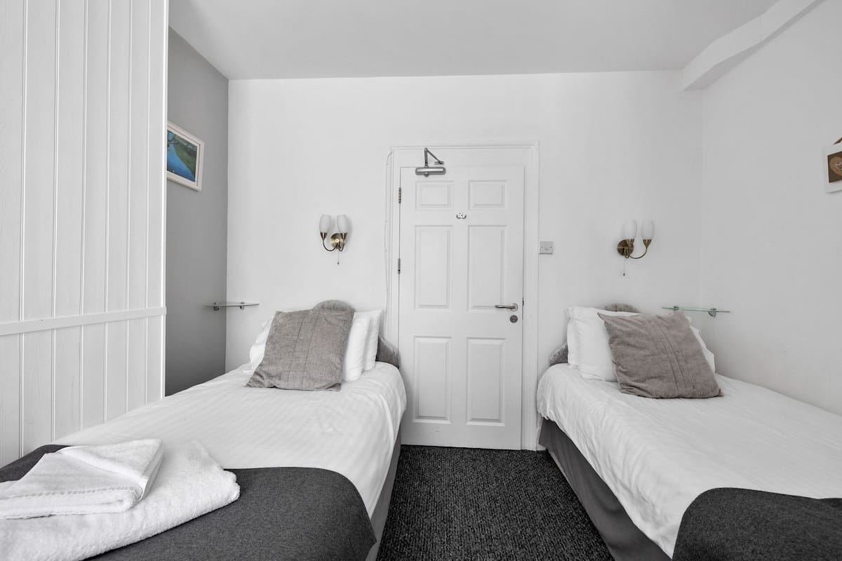 A room with two single beds, white walls, a door, and two wall-mounted light fixtures.