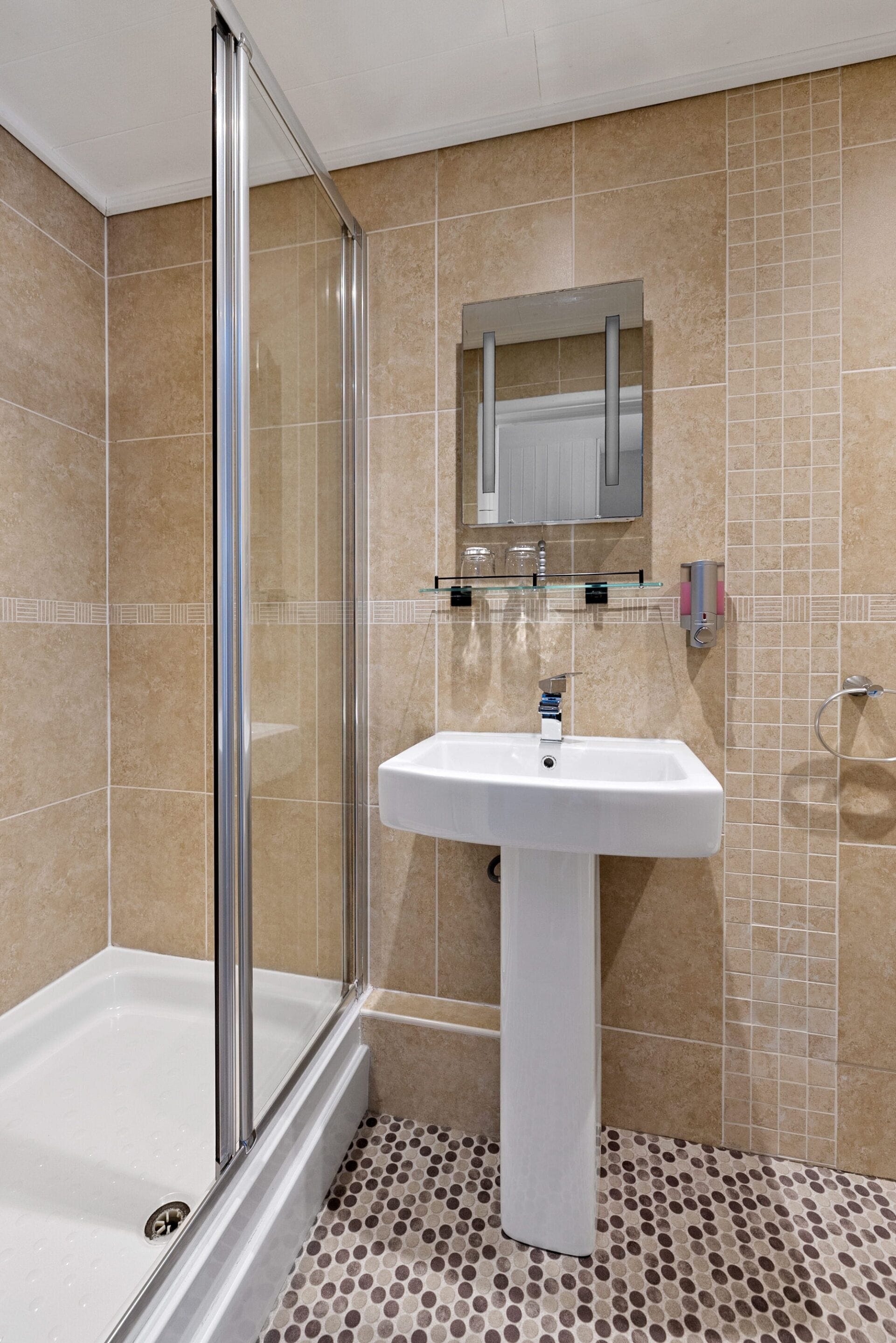 A bathroom with a glass shower enclosure, a white sink, and a tiled floor with a polka dot pattern.
