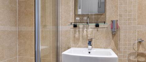 A bathroom with a glass shower enclosure, a white sink, and a tiled floor with a polka dot pattern.