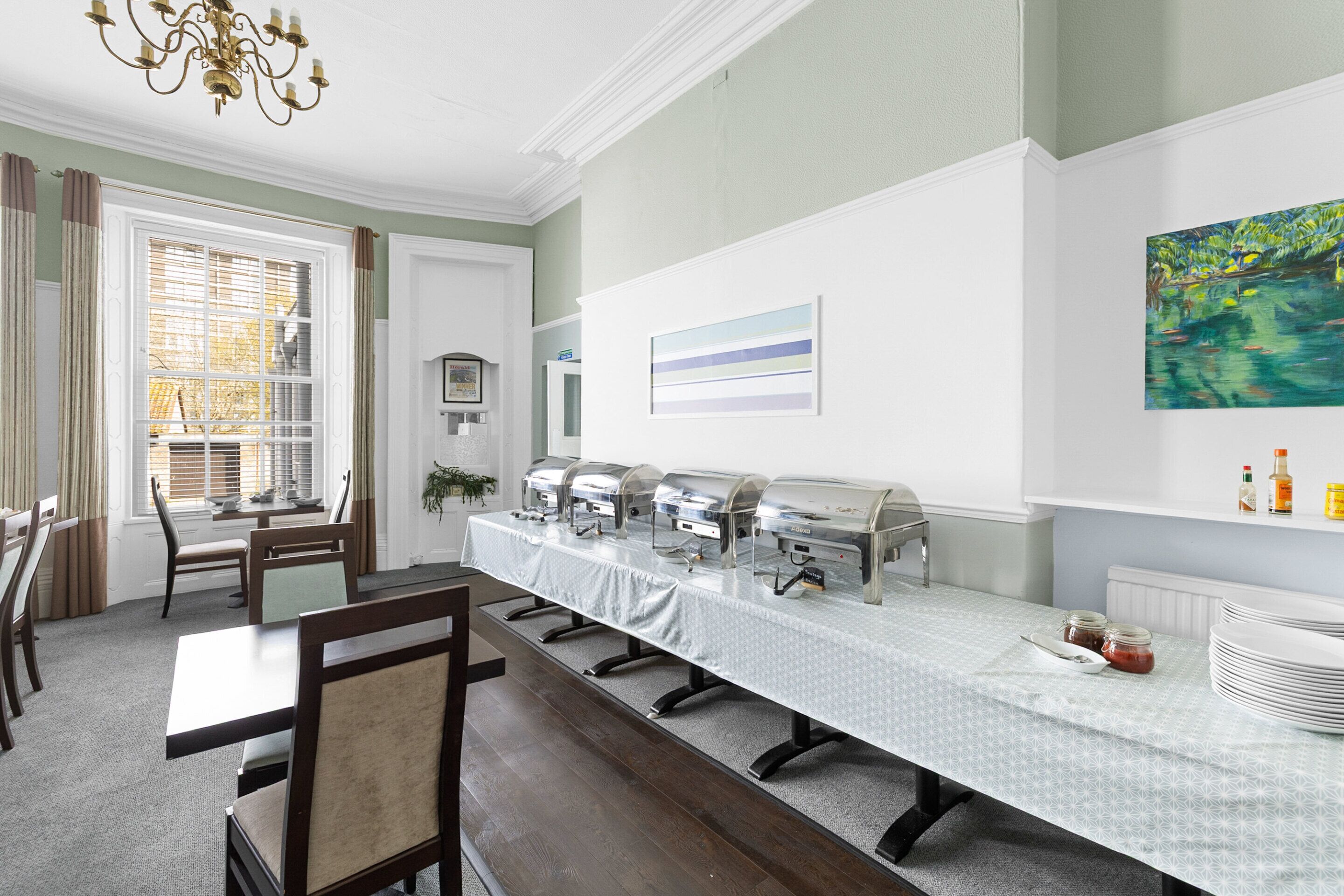 Un espace repas comprenant une longue table, des chaises, des tables de buffet et un tableau accroché au mur.