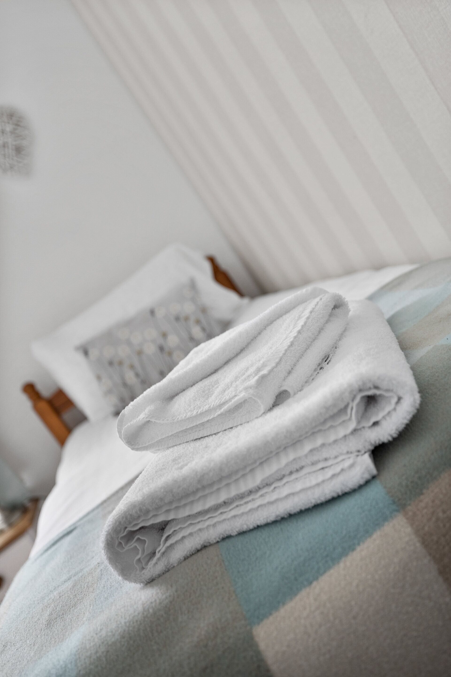 A neatly folded white towel on a checkered bedspread in a room with a wooden headboard and a pillow with a geometric pattern.