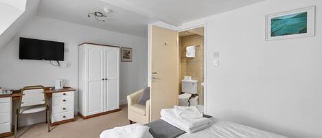 A hotel room with a bed, a desk, a chair, a TV, and a bathroom visible through an open door.