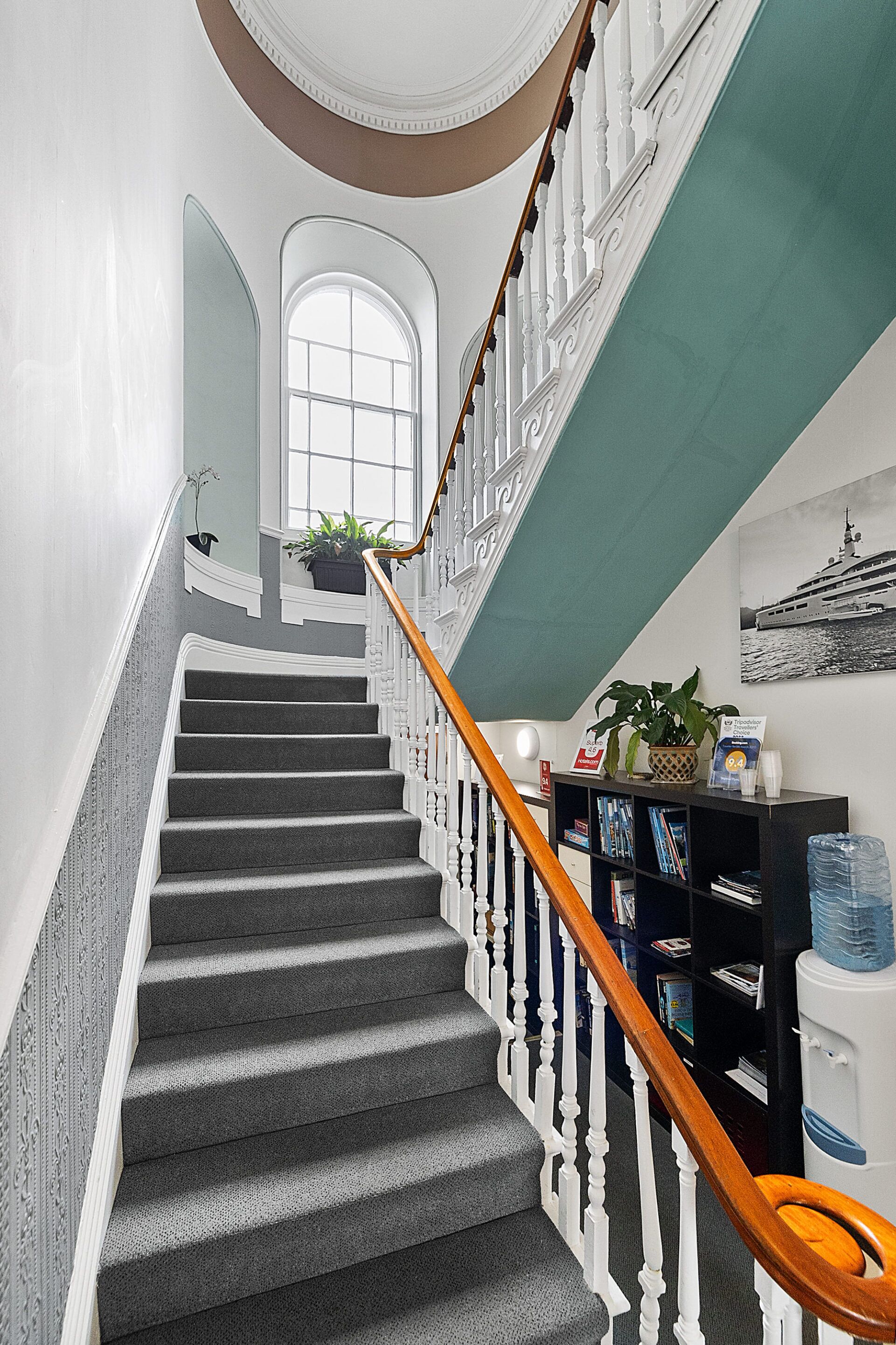 A grand staircase with a wooden handrail, a dark carpeted floor, and a white balustrade.