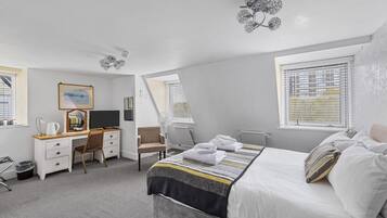 Una habitación de hotel moderna con una cama bien hecha, un escritorio con computadora, una silla y un ventanal con persianas.