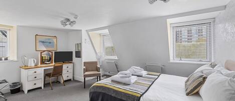A modern hotel room with a neatly made bed, a desk with a computer, a chair, and a large window with blinds.