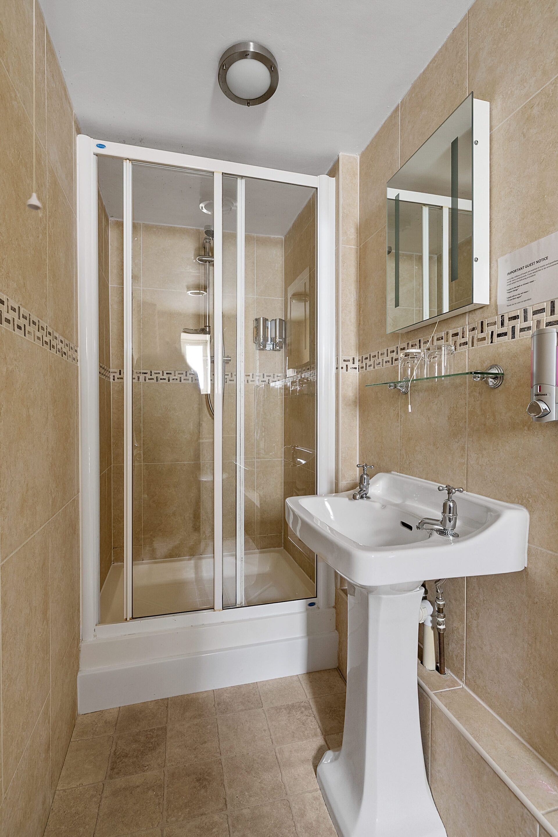 Un baño moderno con ducha de vidrio, lavamanos sobre pedestal y espejo sobre el lavamanos.
