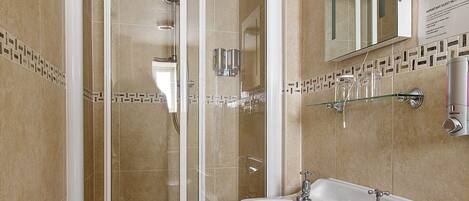 Un baño moderno con ducha de vidrio, lavamanos sobre pedestal y espejo sobre el lavamanos.