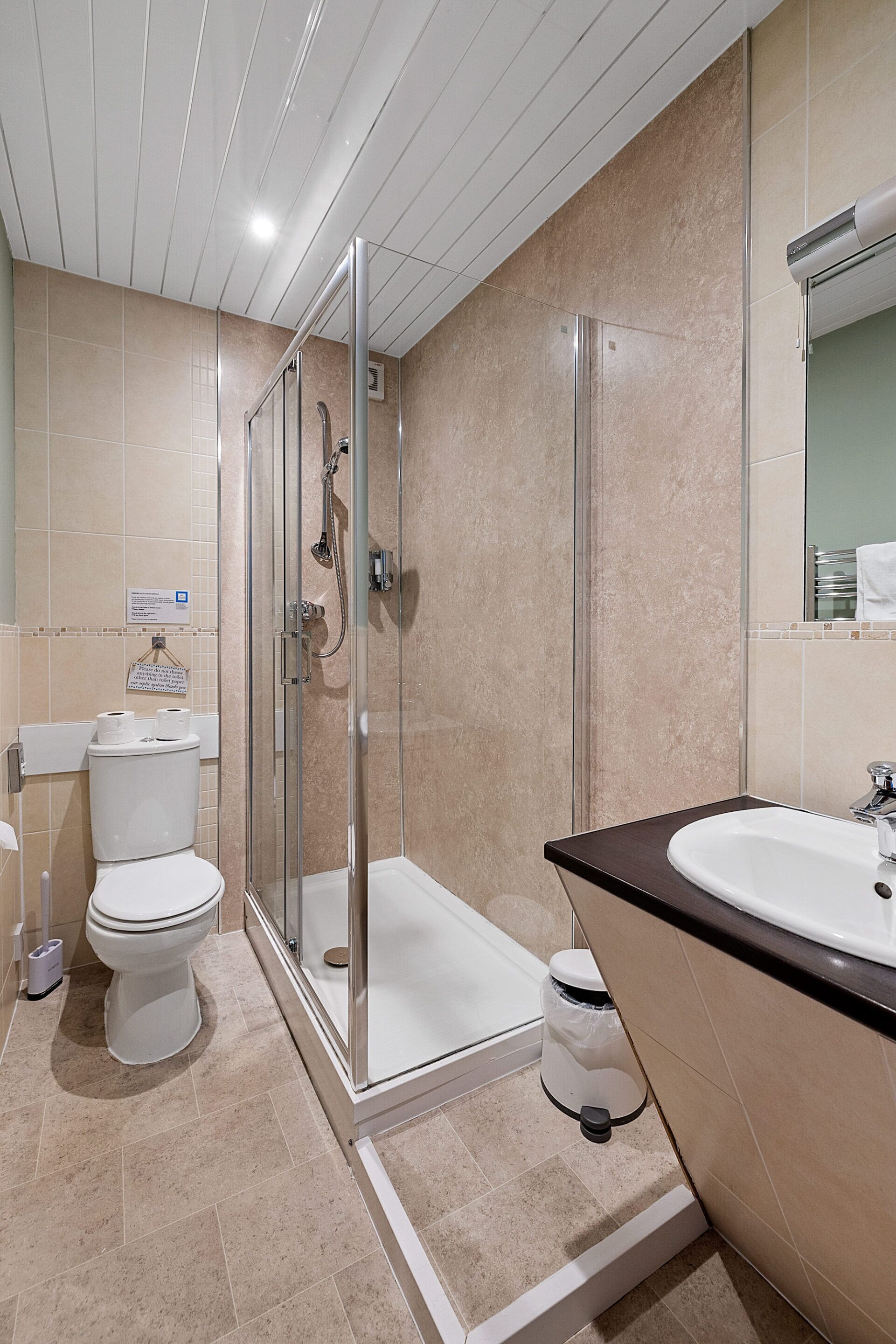 Une salle de bain moderne avec une douche à parois de verre, des toilettes blanches et un lavabo doté d’un plan de travail foncé.