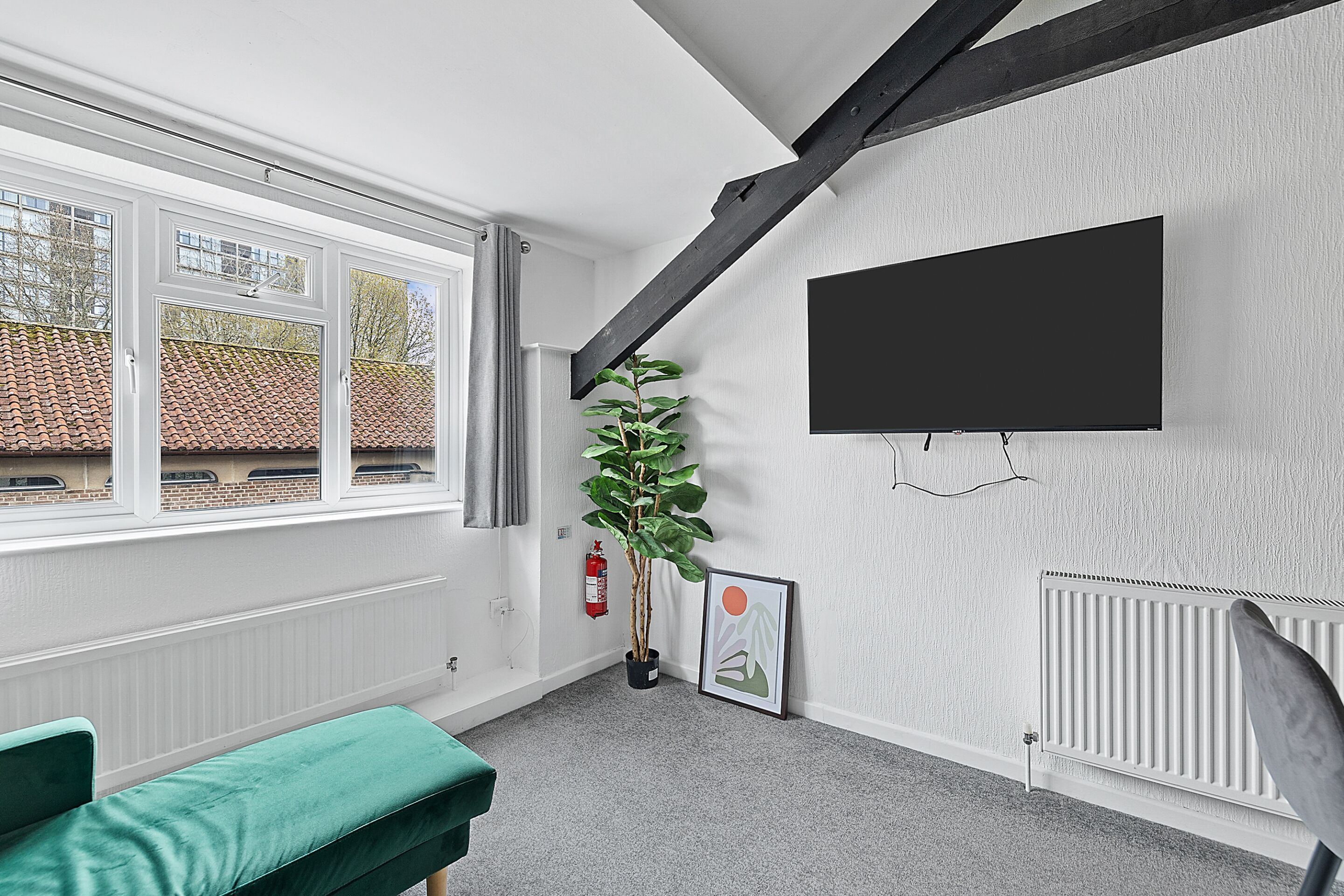 A modern room with a large window, a mounted TV, a potted plant, and a framed picture on the wall.