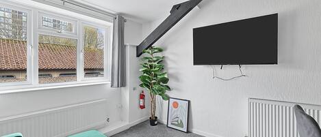 Ein modernes Zimmer mit großem Fenster, einem an der Wand befestigten Fernseher, einer Topfpflanze und einem gerahmten Bild.