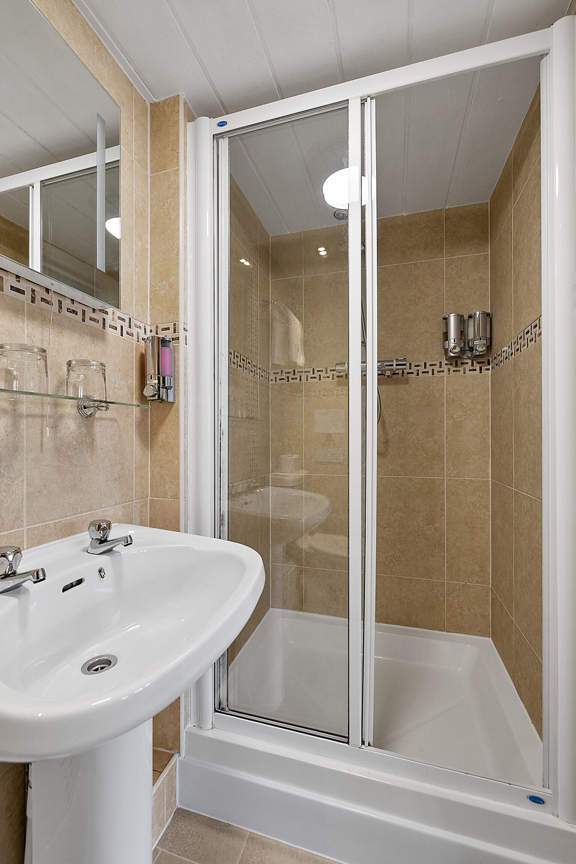 A bathroom with a white sink, a glass shower enclosure, and beige tiled walls.