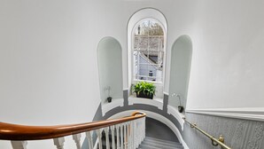 A staircase with white balusters and a wooden handrail, leading to a landing with a potted plant and a view of buildings outside. - Imperial Plymouth (Plymouth)