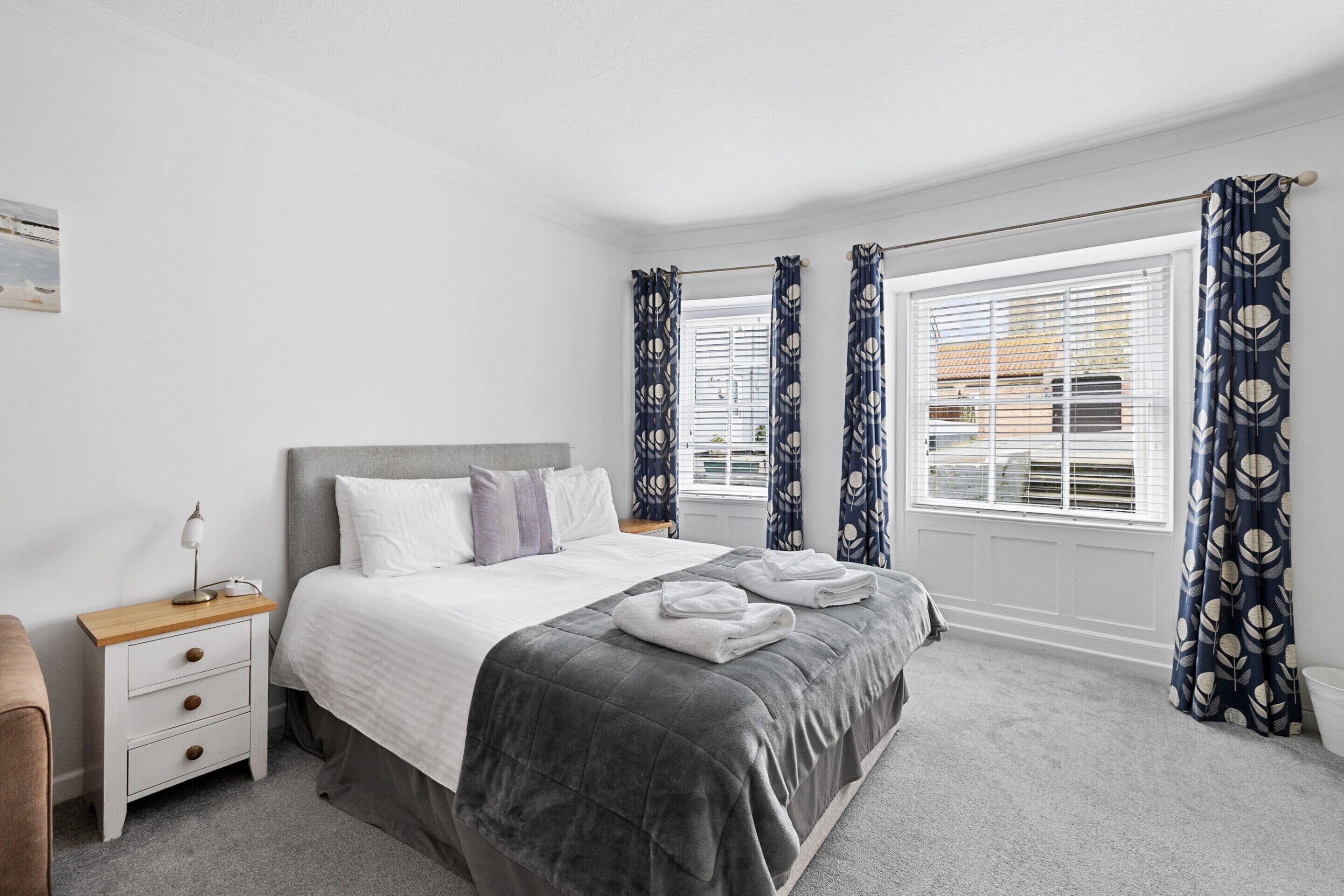 A neatly arranged bedroom with a bed, bedside tables, and a window with curtains.