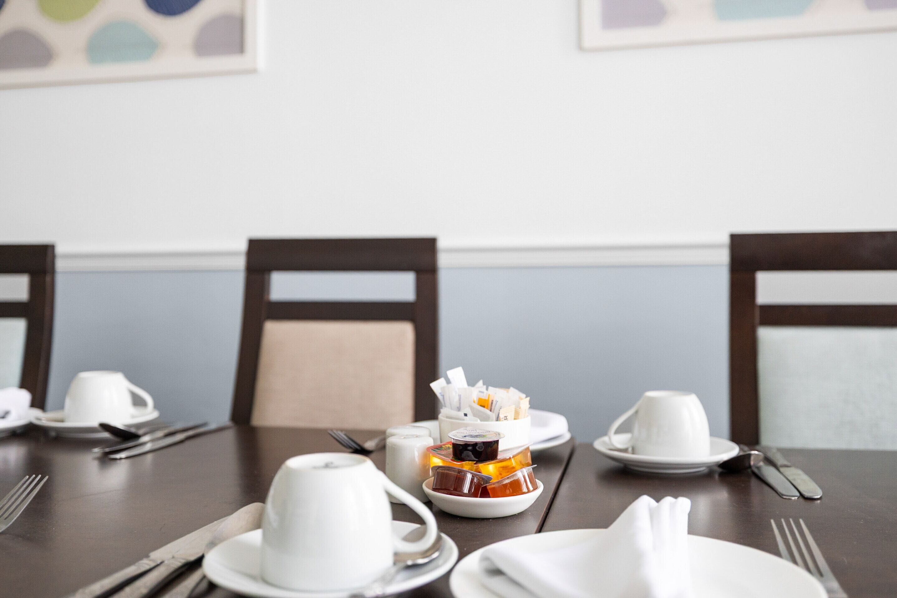 A dining table set with white cups, saucers, and plates, along with condiments and utensils.