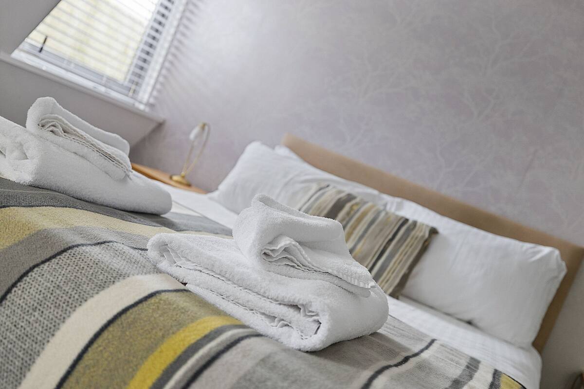 A neatly made bed with white towels, striped bedding, and a bedside lamp.