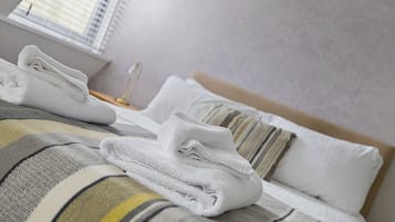 A neatly made bed with white towels, striped bedding, and a bedside lamp.