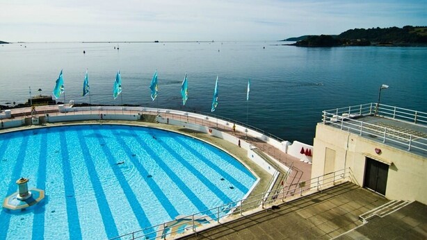 A pool with blue stripes, a deck area, and a view of the water. - Imperial Plymouth (Plymouth)