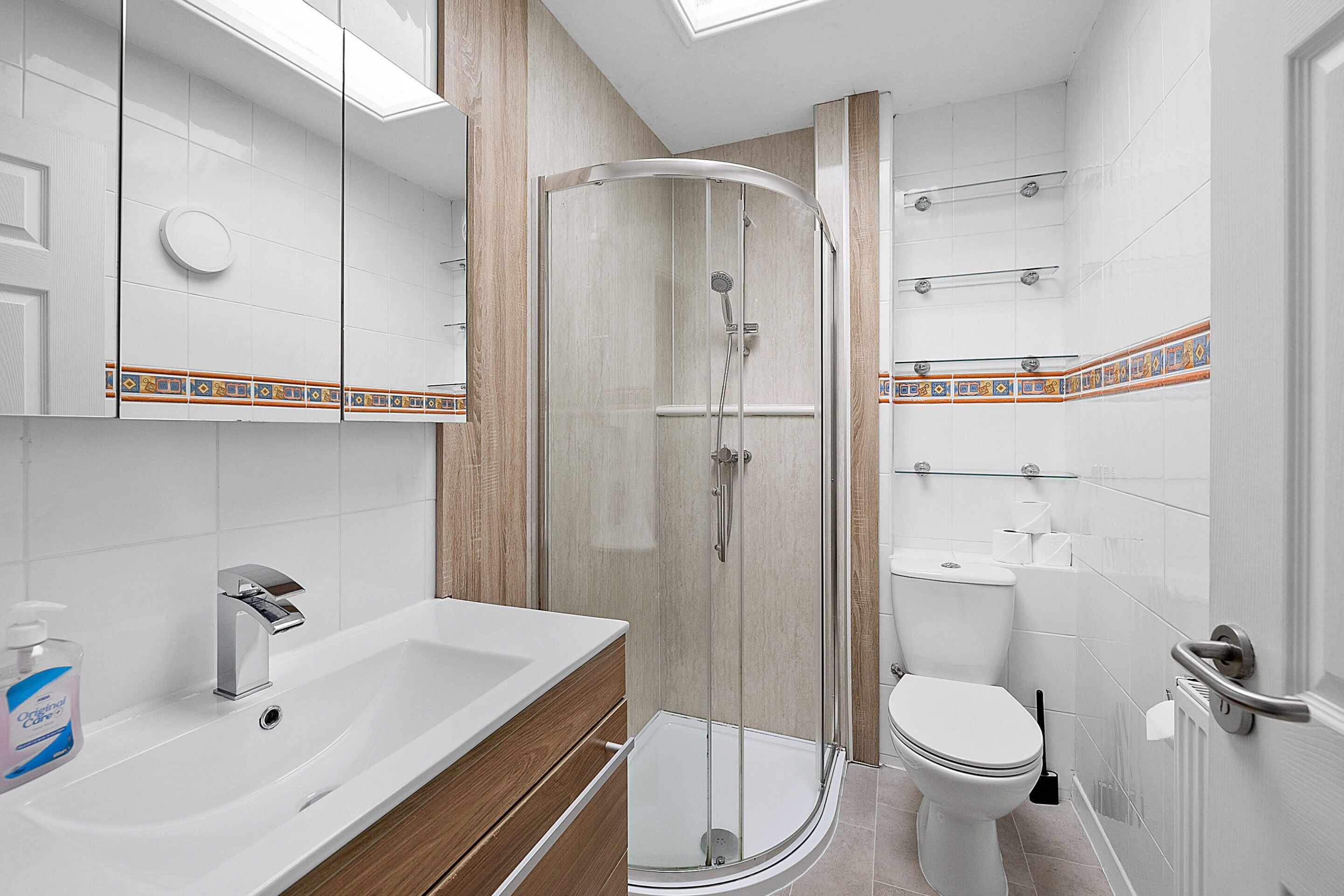 A modern bathroom with a glass shower enclosure, a sink with a wooden vanity, and a toilet.