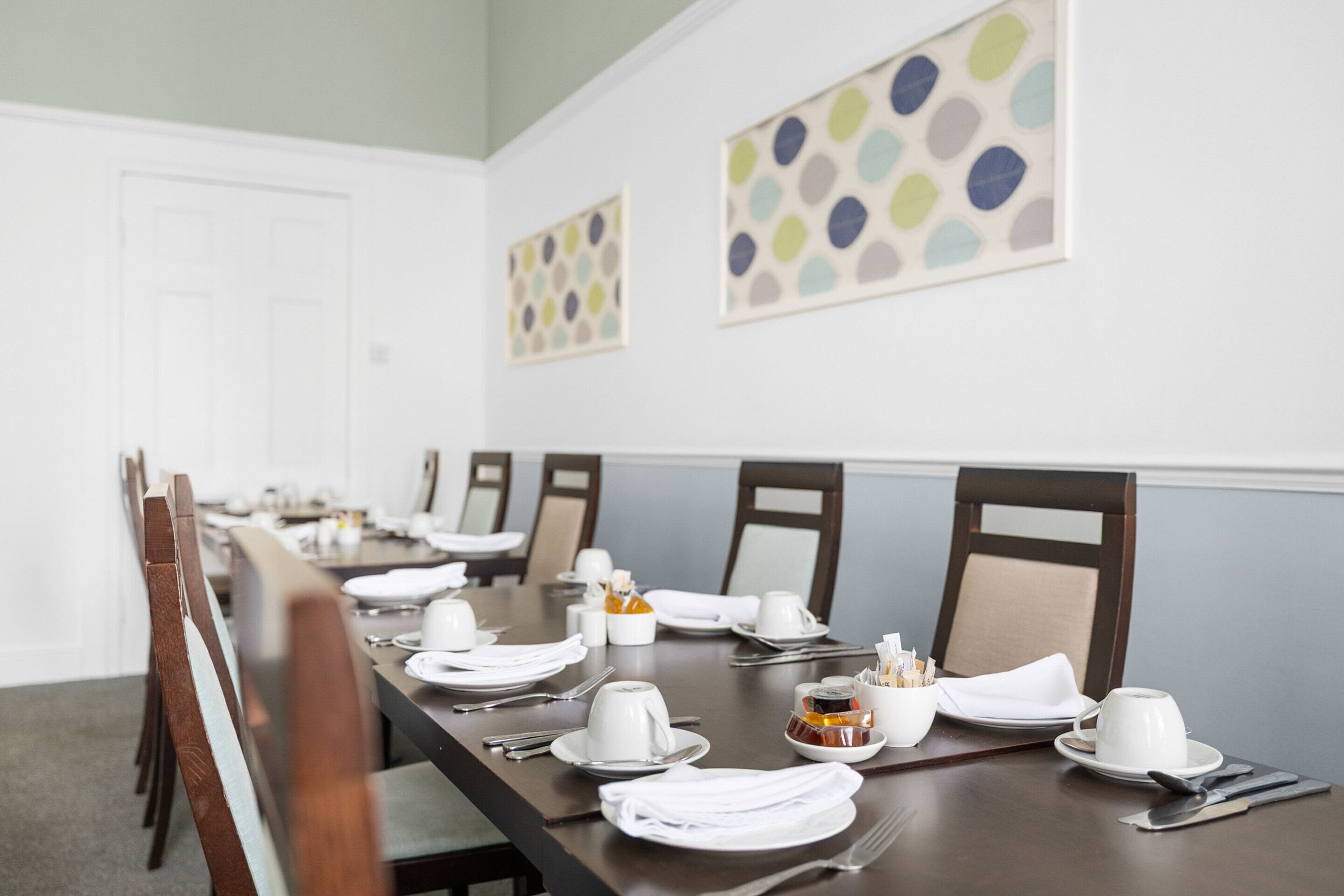A dining table set for a meal with chairs, plates, cutlery, and a salt and pepper set.