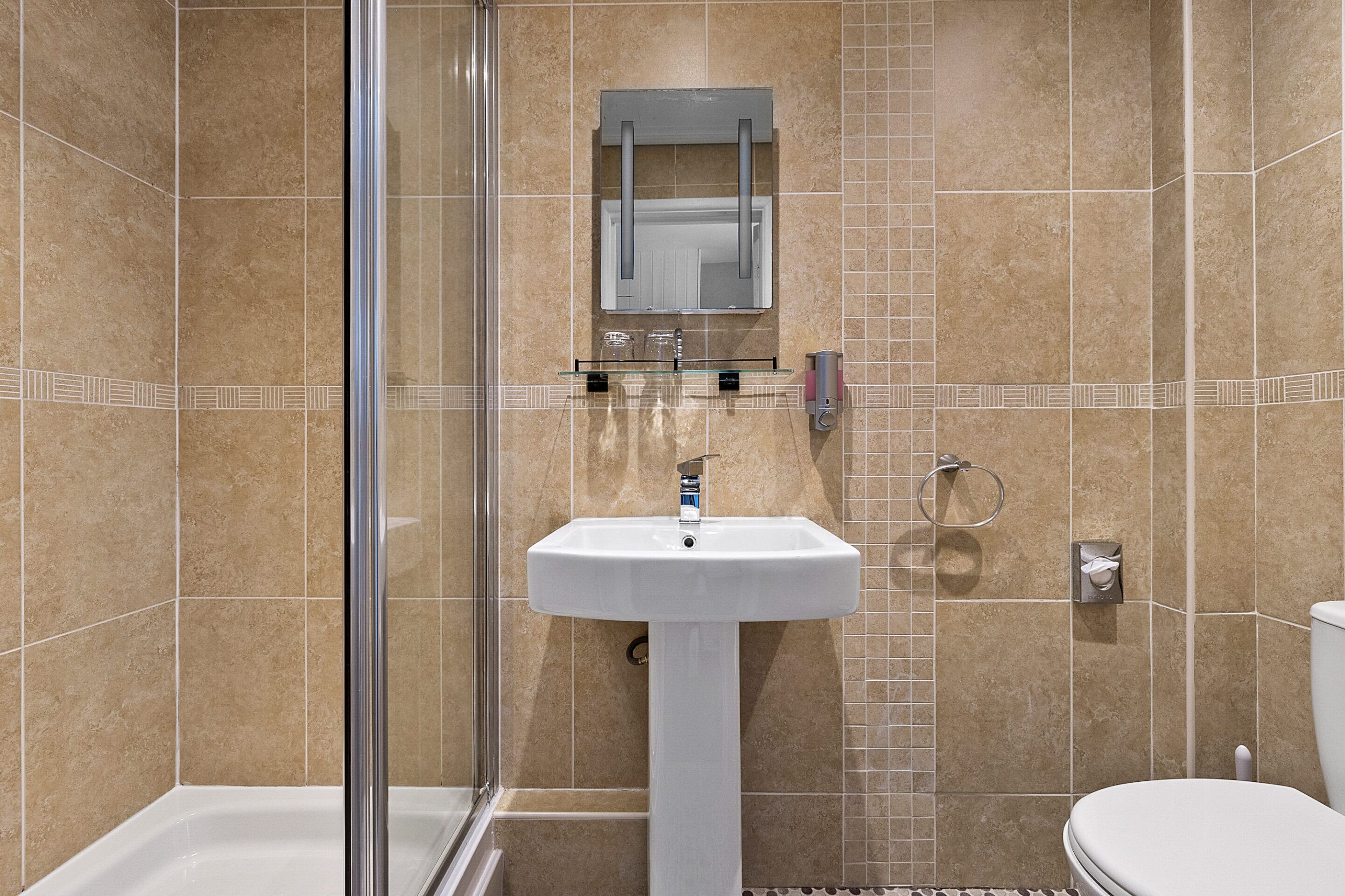 A bathroom with a glass shower enclosure, a white pedestal sink, and a toilet.
