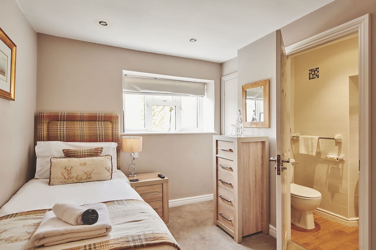 A bedroom with a bed, bedside table, dresser, and a bathroom with a toilet and shower.