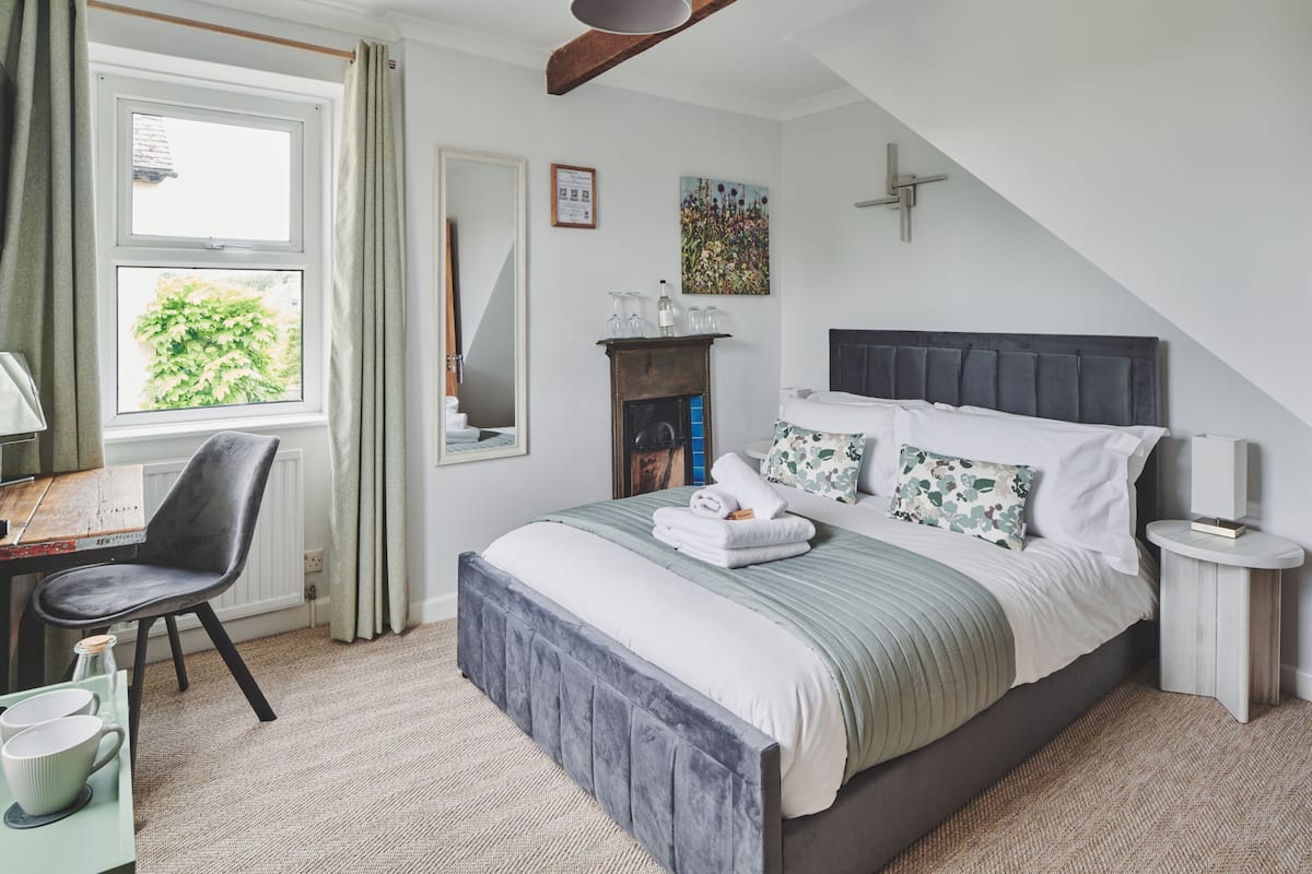 A bedroom with a bed, a chair, a table, and a window with curtains.