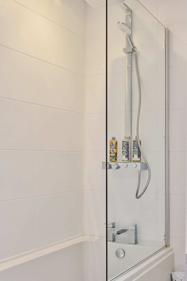 A modern shower enclosure with a glass door, a handheld showerhead, and two bottles of shampoo on a shelf.