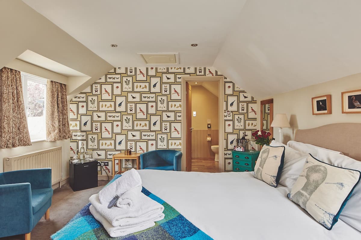 A hotel room with a large bed, a blue armchair, a small desk, and a wall decorated with framed pictures.