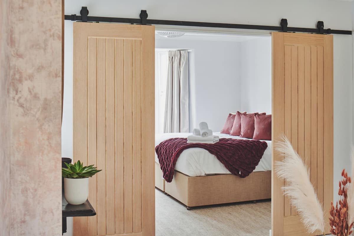A bedroom with a wooden wardrobe, a bed with a red blanket, and a potted plant.