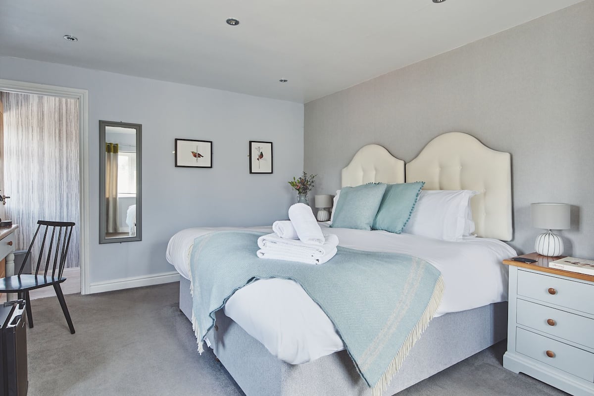A bedroom with a bed, bedside table, chair, and a mirror.