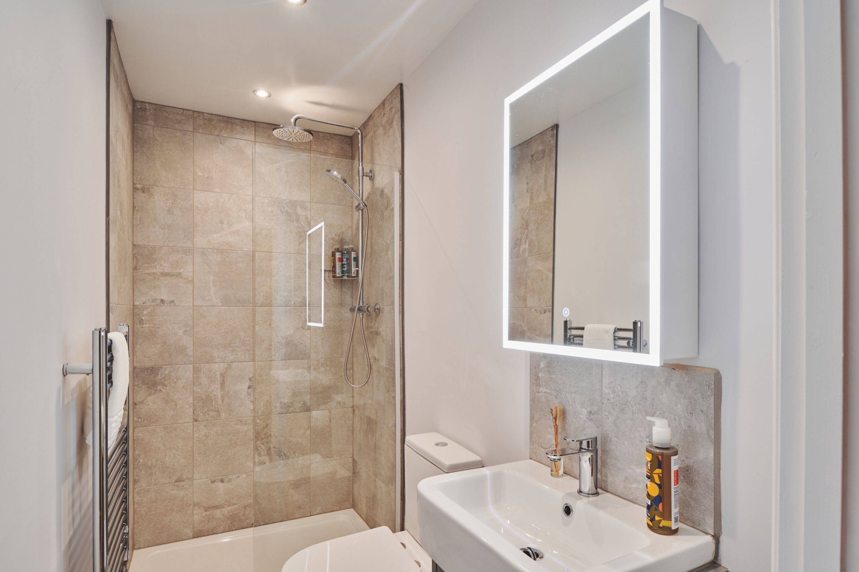 A modern bathroom with a glass-enclosed shower, a white sink, and a large mirror.