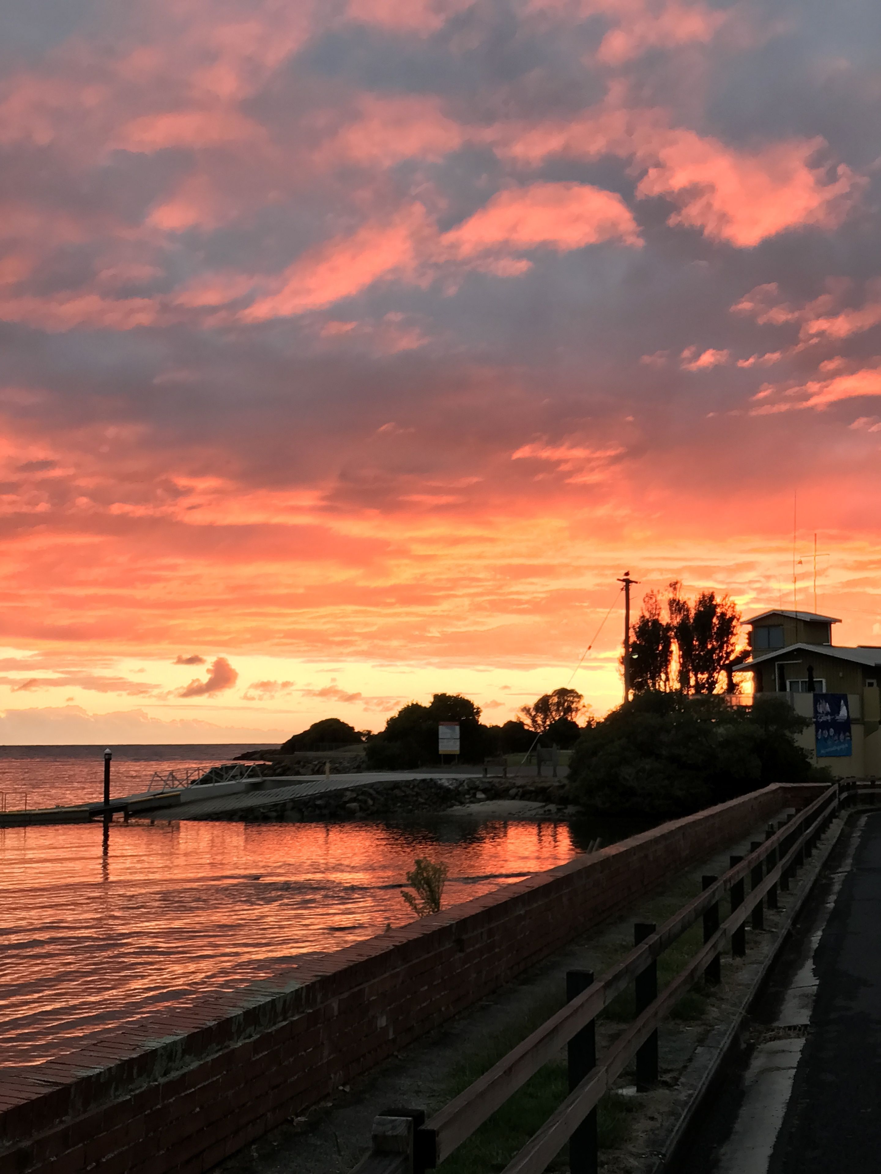 Ein Sonnenuntergang über einem Ufer mit einer Backsteinmauer und einem Holzsteg.