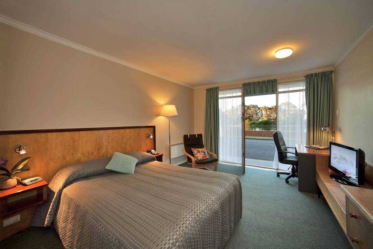 Habitación de hotel con cama, escritorio, silla, televisor, lámpara y vistas al exterior.