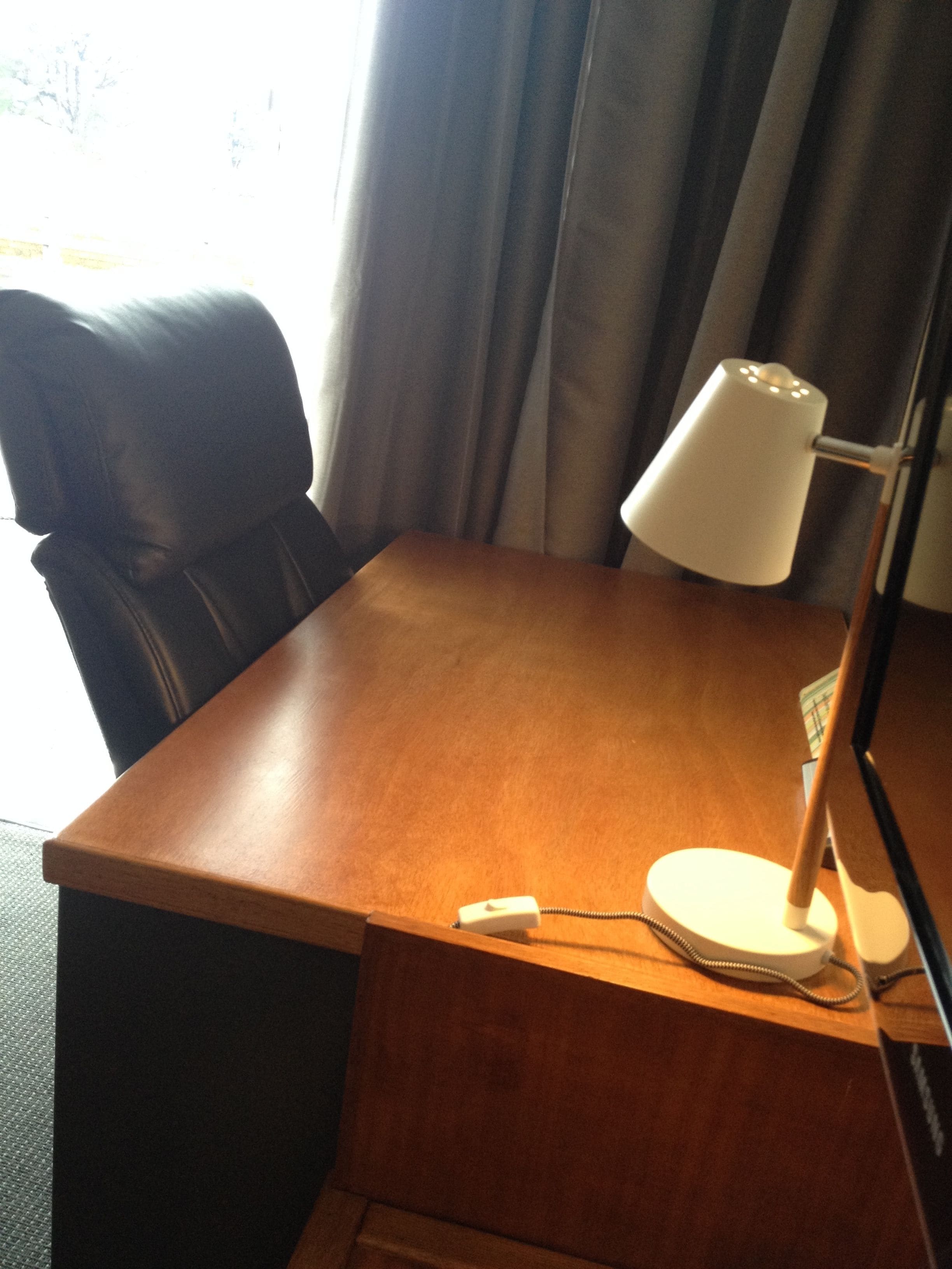 Een houten bureau met een witte lamp, een telefoon en een stoel.